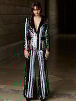 Model wearing Jovani M02942, a multi-colored sequin pantsuit with a deep V-neckline and flared pants.