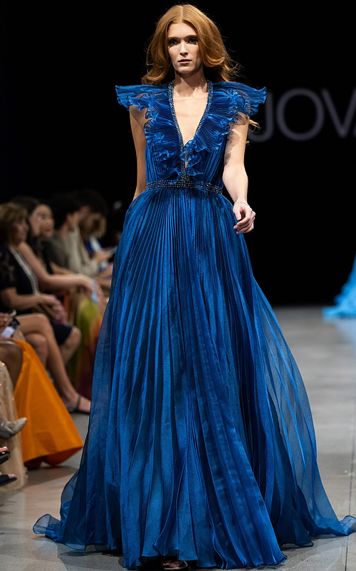 Model wearing Jovani S22362 elegant blue dress with deep V-neckline, ruffled details, and flowing A-line silhouette.
