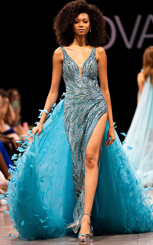 Model wearing Jovani S23074 blue gown with feather-like back details.