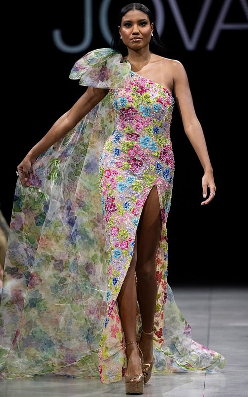 Model wearing Jovani S37492 multi-color floral gown seen from the back with a dramatic cape detail.