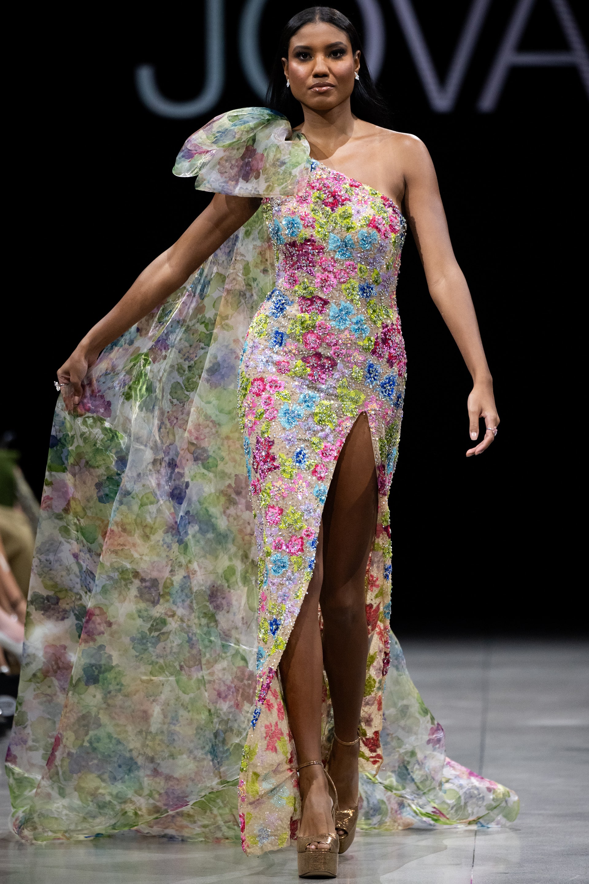 S37492.jpg Model wearing Jovani S37492 multi-color floral gown seen from the back with a dramatic cape detail.