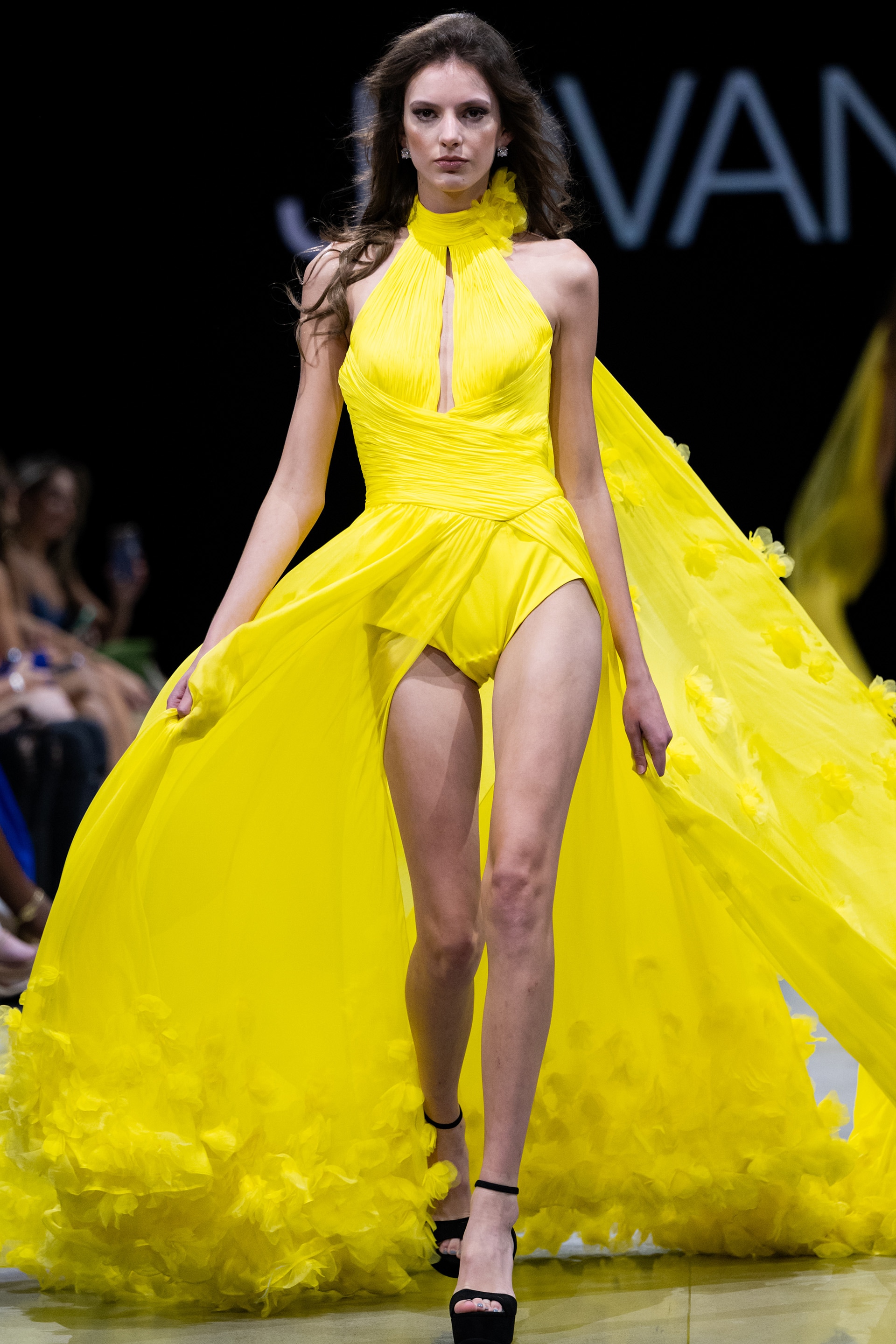 S38104.jpg Model wearing Jovani S38104 yellow gown with halter neckline and flowing cape, front view.