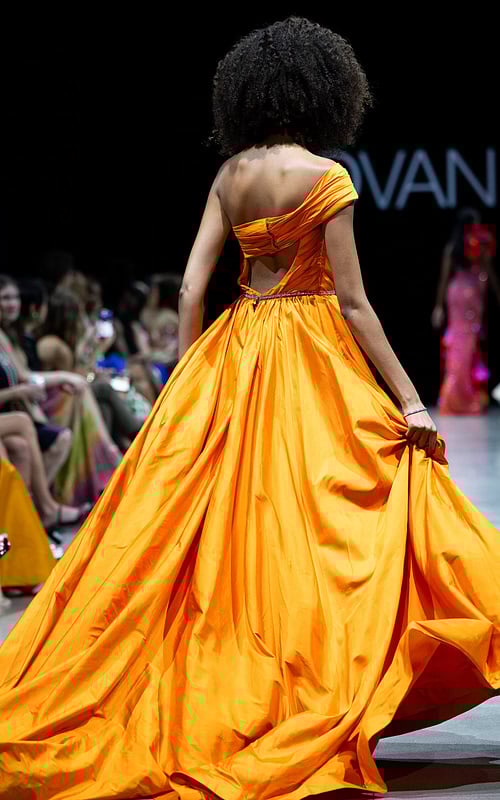 Back view of model wearing S38441 orange gown with flowing skirt