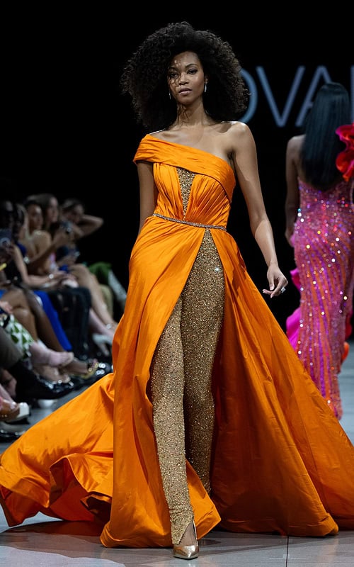Model wearing S38441 orange gown with off-the-shoulder neckline and high slit