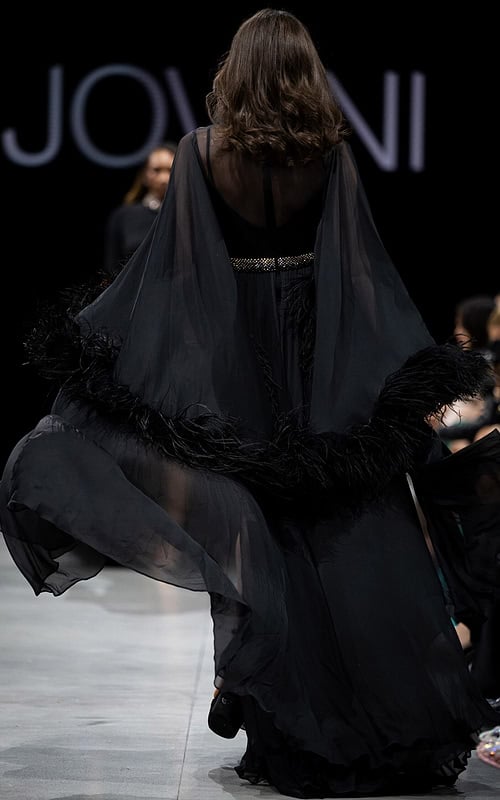 Model wearing S39276 black gown, back view with sheer feathered sleeves.