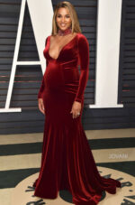 Model wearing Jovani S55169 burgundy velvet gown with deep V-neckline and long sleeves.